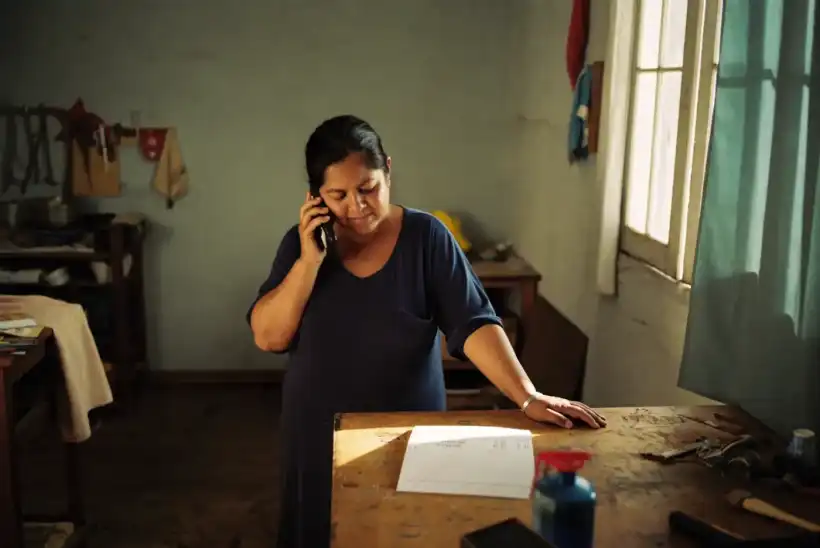A woman in her workshop checks her phone next to a printed invoice on the workbench